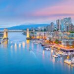 The city of vancouver at dusk with boats docked in the harbor.