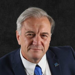 Governments Must Address The Need For Substantially More Purpose-built Rental - Canadian Real Estate Wealth A man with gray hair wearing a white shirt, blue tie, and dark suit jacket against a dark background.