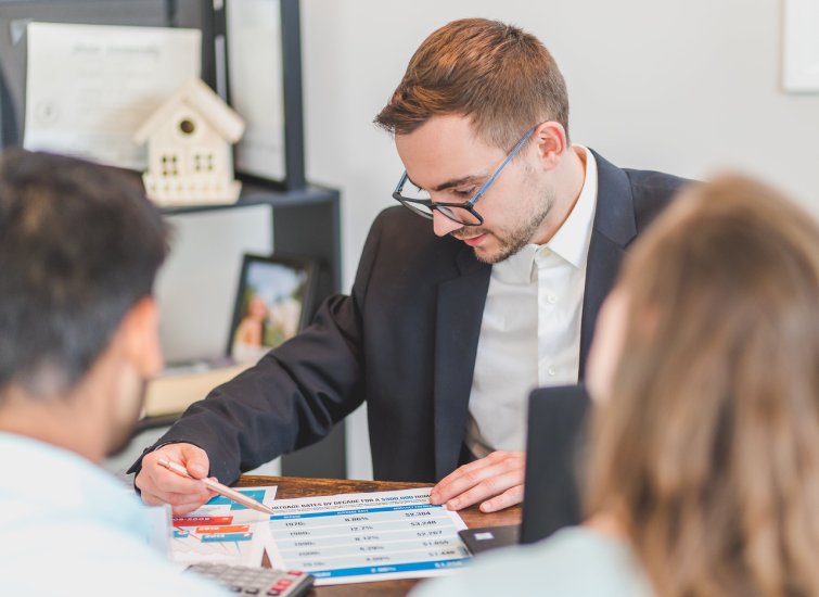 A man in a suit is discussing real estate with a group of people at a table.
