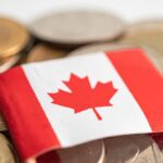 A small Canadian flag lies on a pile of various coins.